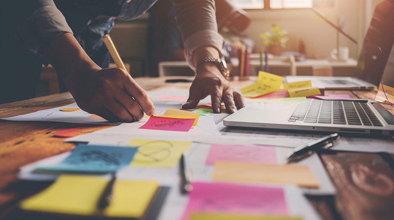 An individual intensely brainstorming at a cluttered desk full of colorful sticky notes and documents, symbolizing creativity and busy work environment.