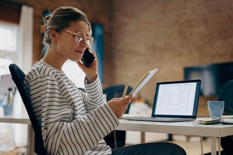 Young female architect is talking phone with colleague and looking on notepad